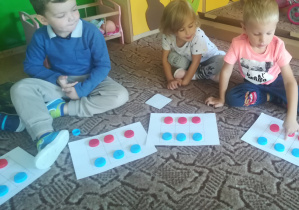 Dzieci umieszczają plastikowe czerwone i niebieski nakrętki na kwadracie-planszy do kodowania